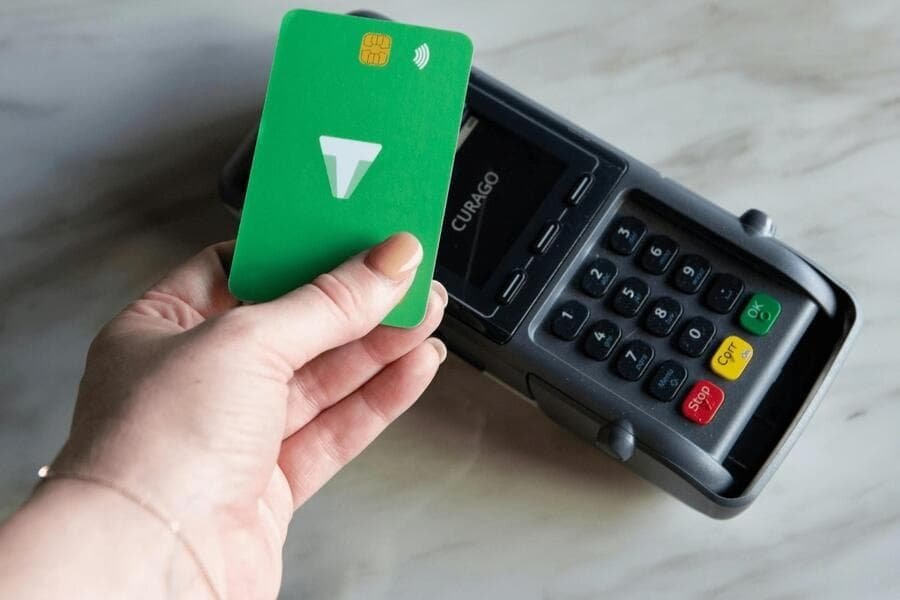 Credit Cards; Hand holding a green credit card making a contactless payment on a modern card reader terminal.