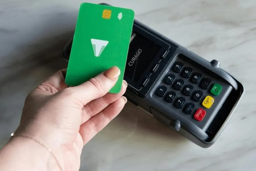 CreditCards101post Credit Cards; Hand holding a green credit card making a contactless payment on a modern card reader terminal.