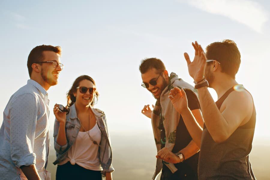 Group of young adults laughing and enjoying time together outdoors at sunset.