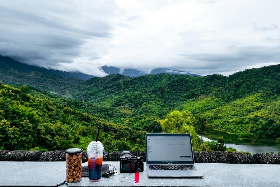 Laptop on an outdoor table overlooking green mountains, representing a freedom lifestyle of traveling, working less, and building wealth.