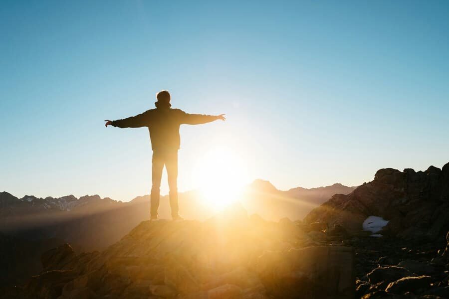 freedom Person standing on a mountain at sunrise symbolizing financial freedom.